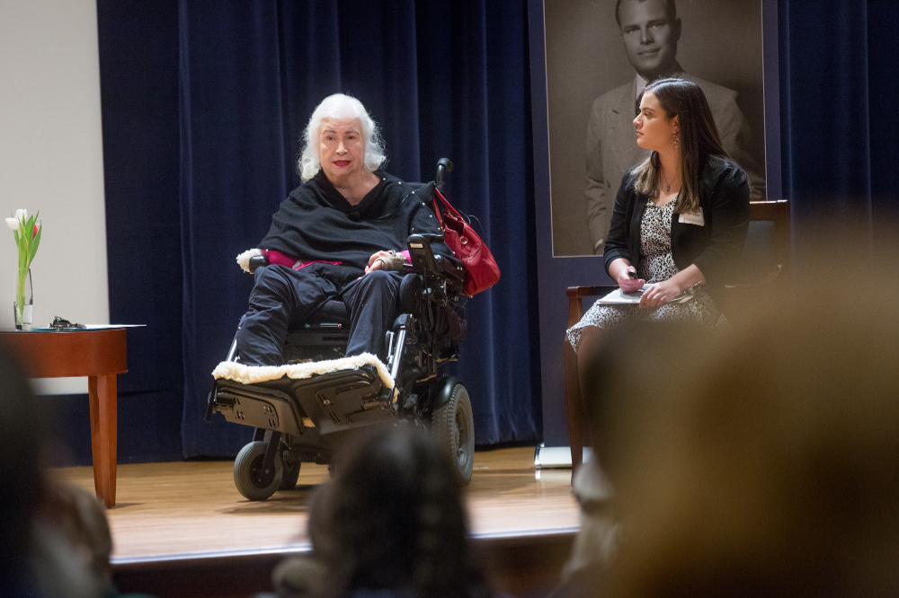 woman in wheelchair on stage, a woman seated to her left