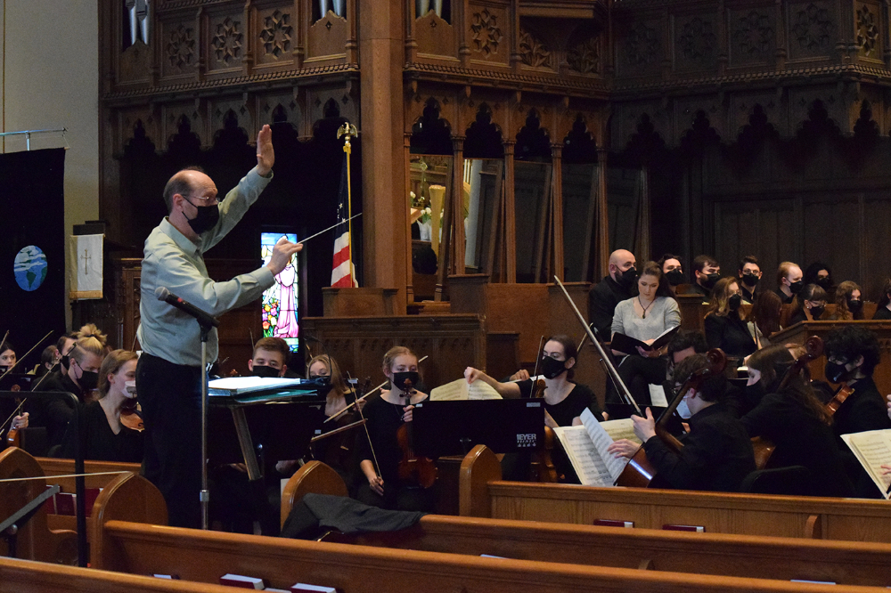 Henry Duitman conducts musicians seated before him in a church