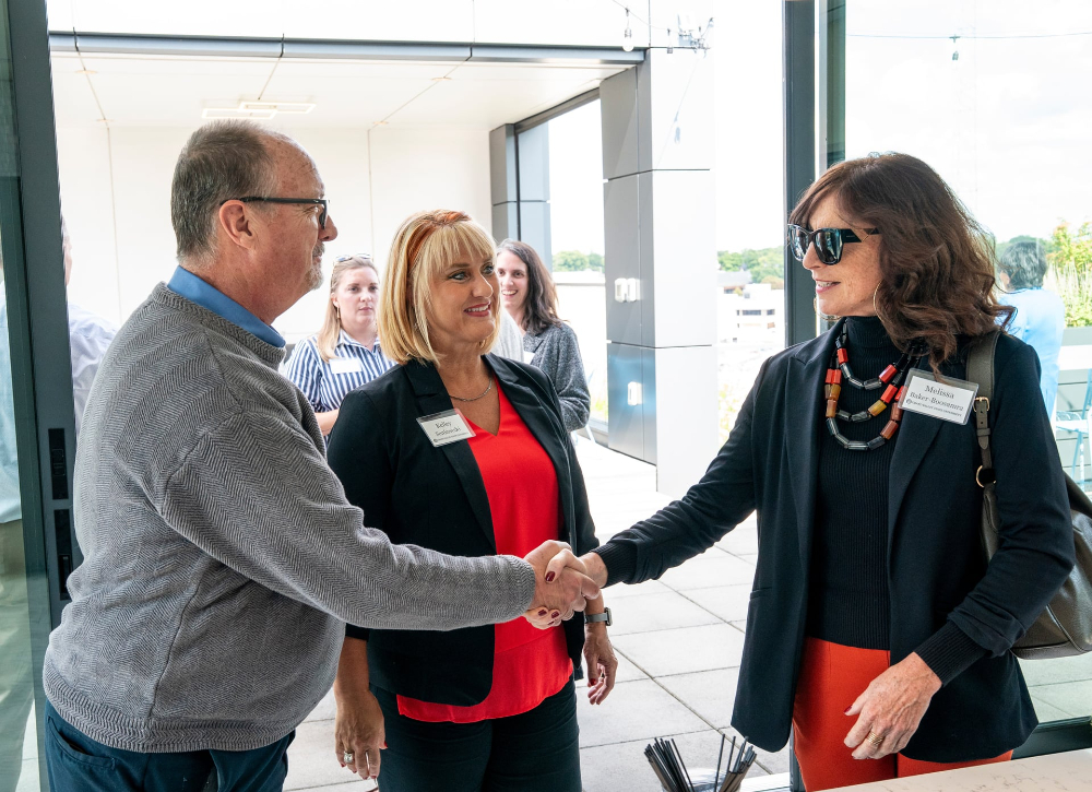 three people standing, man on left and woman on right shaking hands