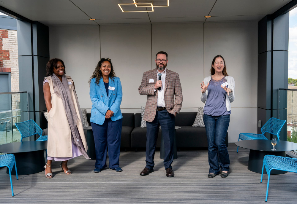 four people standing, man holding a microphone