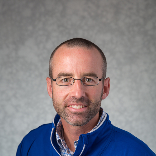 headshot of Jon Coles, who is dressed in GV quarter-zip shirt with button down underneath it. He is wearing glasses