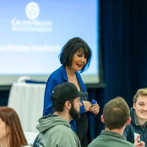 President Mantella talks with students seated at a table while she stands in a blue jacket