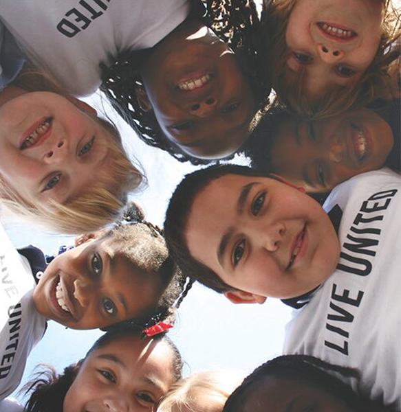 group of kids in a huddle looking down at a camera. They are wearing Live United shirts.