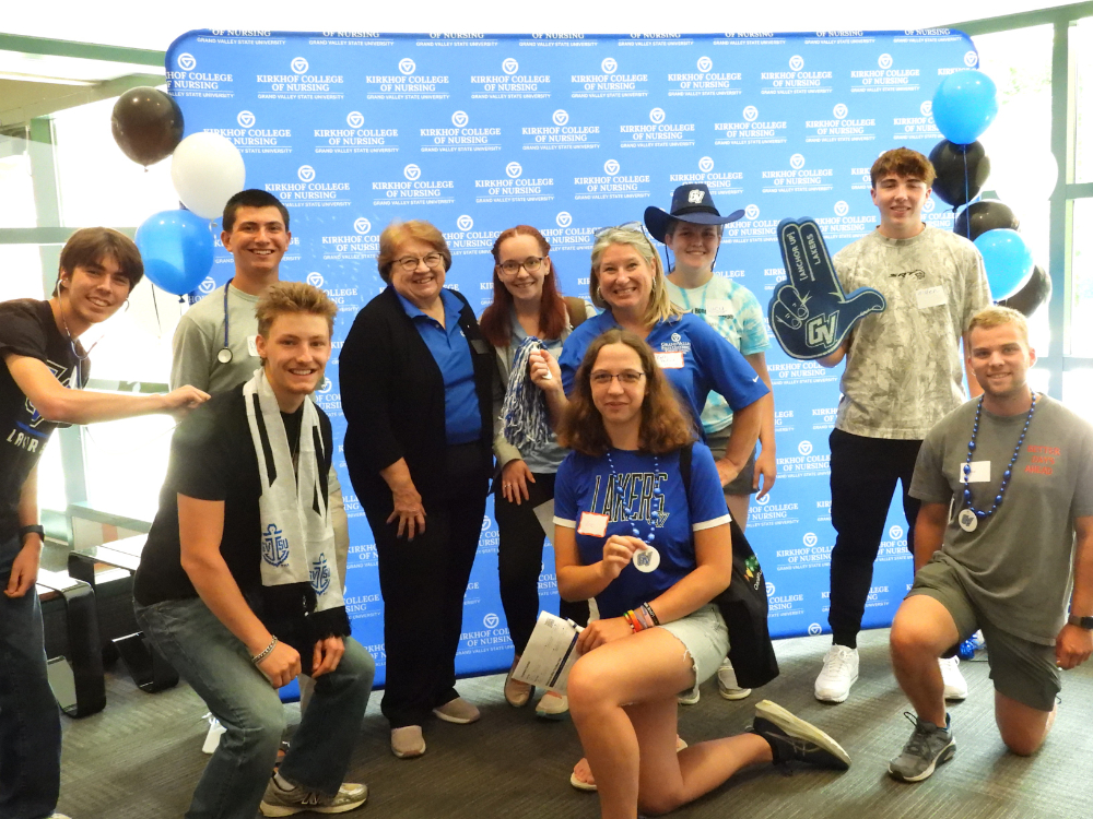 students and nursing dean Linda Lewandowski stand and pose in front of a backdrop with Kirkhof College of Nursing, students wearing or holding photo props