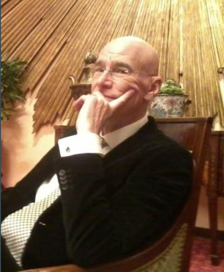 Mack Smith seated in a chair in dark jacket, white shirt and tie