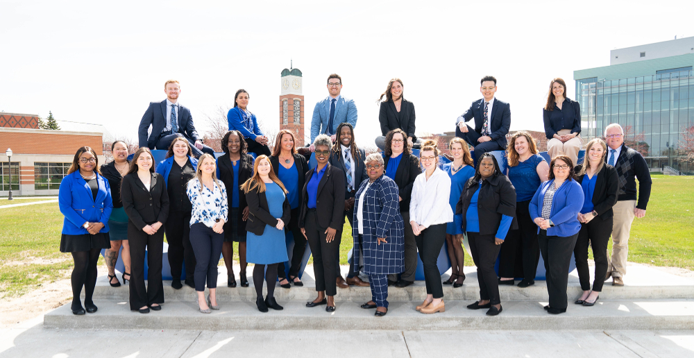 Human Resources staff members, many in blue, black or white, stand near or sit on the GVSU letters.
