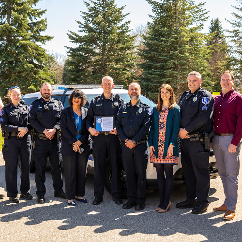 group of people standing, some police officers; officer in middle holding a framed certificate. President Mantella stands in center. They are outside the Facility Services building.