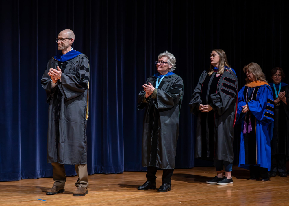five people in academic regalia on stage in line to receive awards