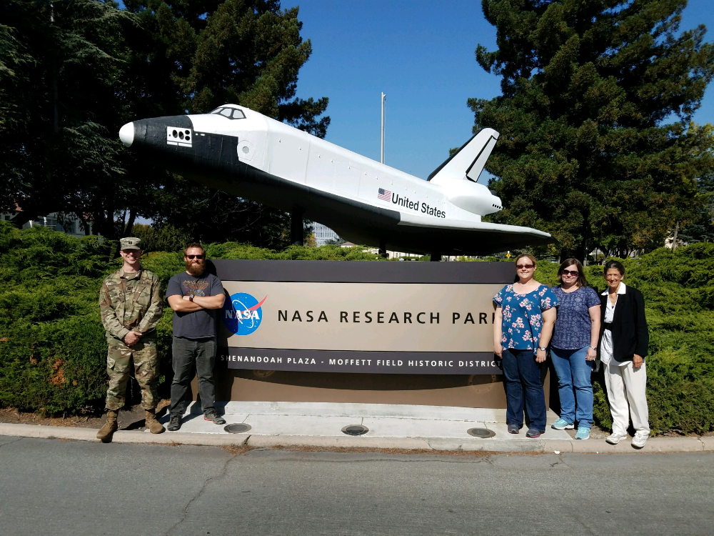 people on either side of a sign NASA Research Park with a space shuttle mounted to the sign