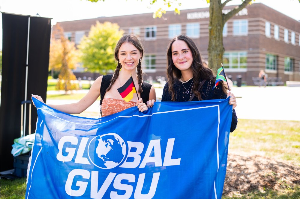 two students hold Global GVSU flag in front of Kirkhof Center