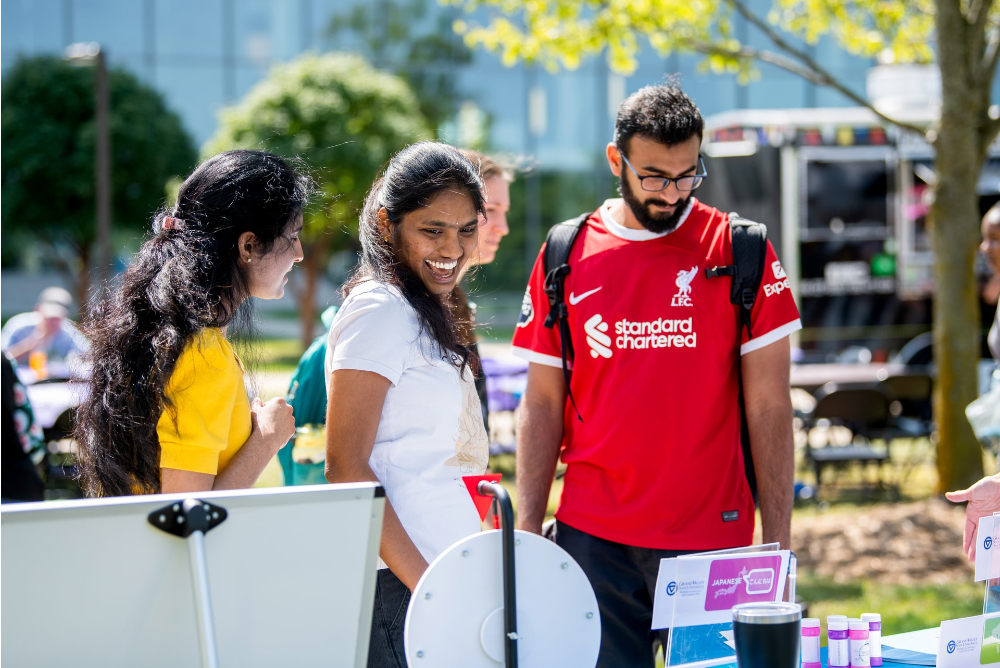 3 students look at a tabling event outside on the Kirkhof Center lawn