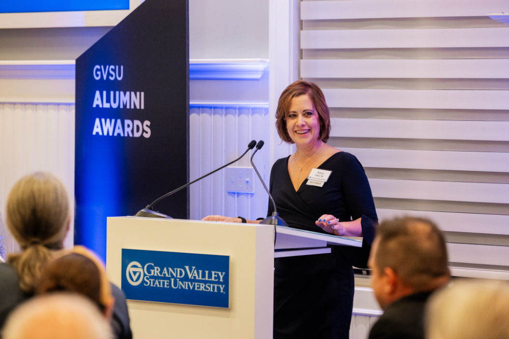Joyce Ohm at podium, vertical banner: GVSU Alumni Awards