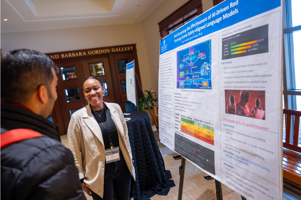 student in front of poster explaining research to a man in winter coat outside the Gordon Gallery in the DeVos Center
