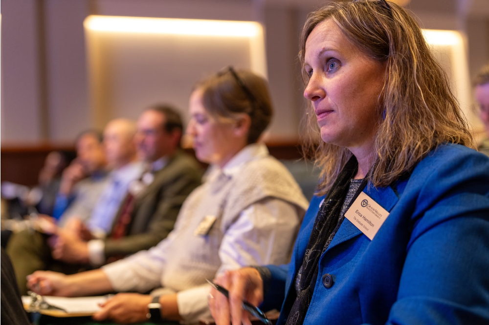 Erica Hamilton in blue jacket seated at end of row of people seated and taking notes