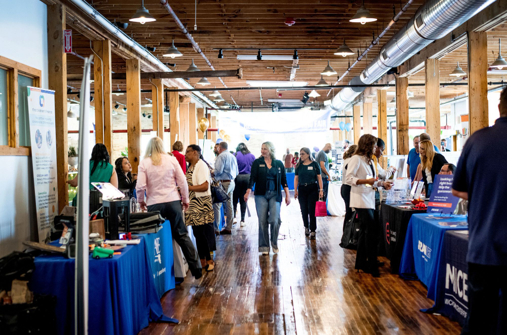 hallway showing tabling, with banners draped over tables, people walking down center aisle