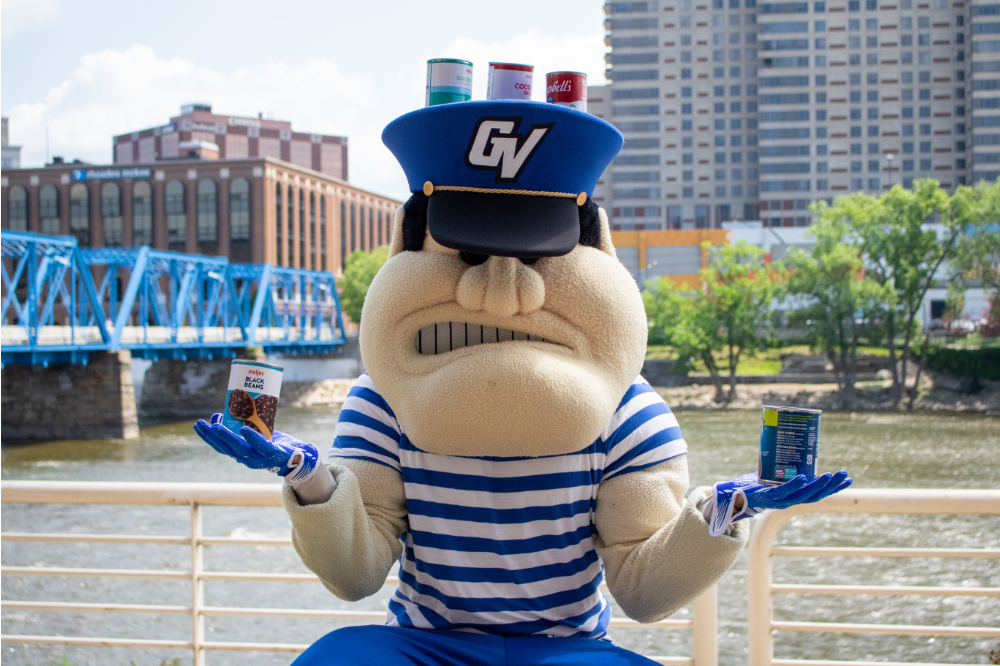 Louie the Laker holds a canned food item in each hand in front of the Blue Bridge in Grand Rapids