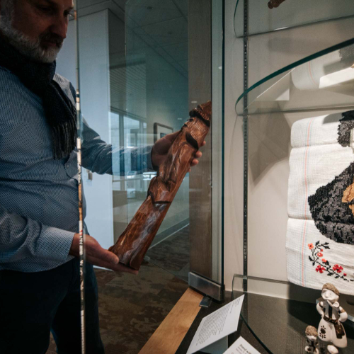 man wearing scarf places a wooden piece of artwork in a display case