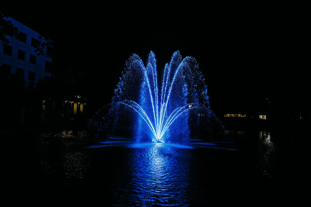 fountain in Zumberge Pond lit up blue against black night sky