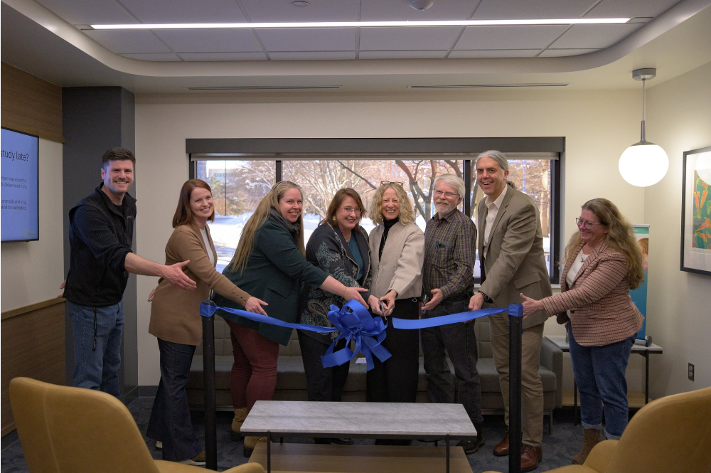 eight people behind a blue ribbon with scissors ready to cut it