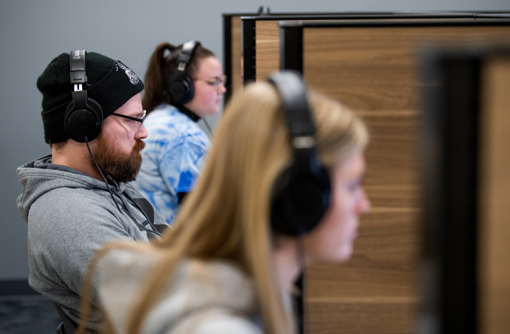 Three students with headphones on in a lab separated by wooden partitions