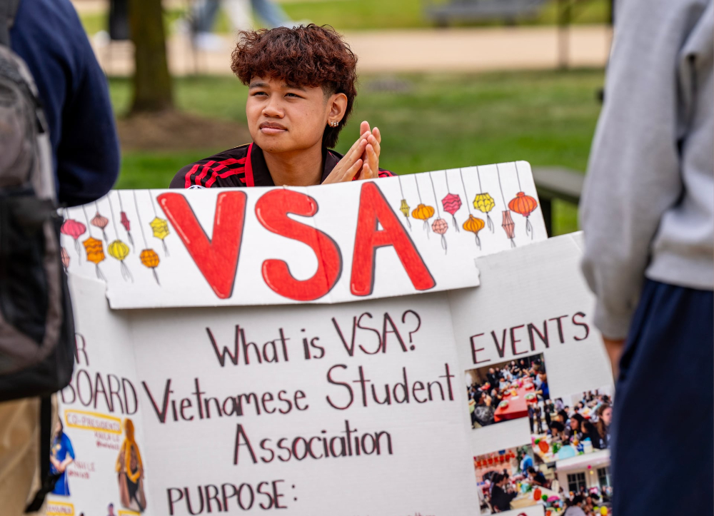 student Kevin Nguyen sits behind a poster for the Vietnamese Student Association