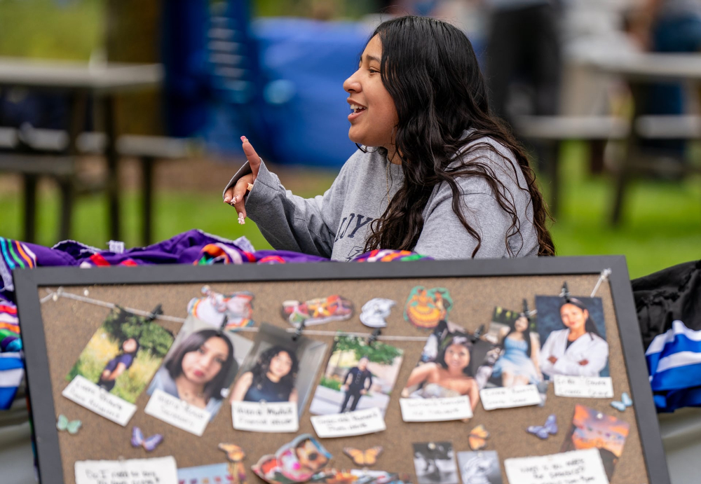 Emma Ramos sits behind a corkboard with photos on it at the fair