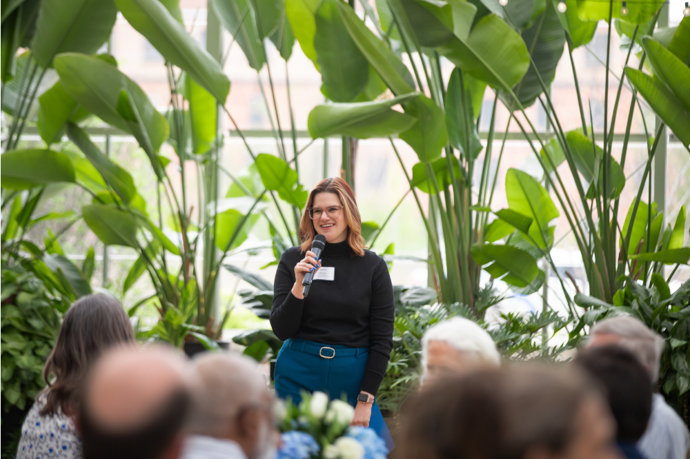 Laura Aikens speaks with a microphone in a greenhouse at the Grand Rapids Downtown Market