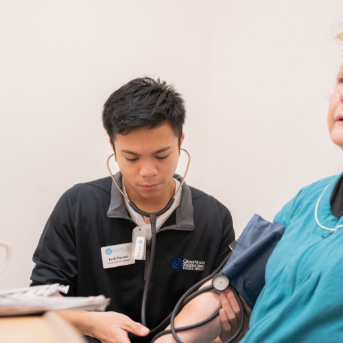 student with stethoscope and blood pressure cuff takes the reading of an elderly woman both are seated