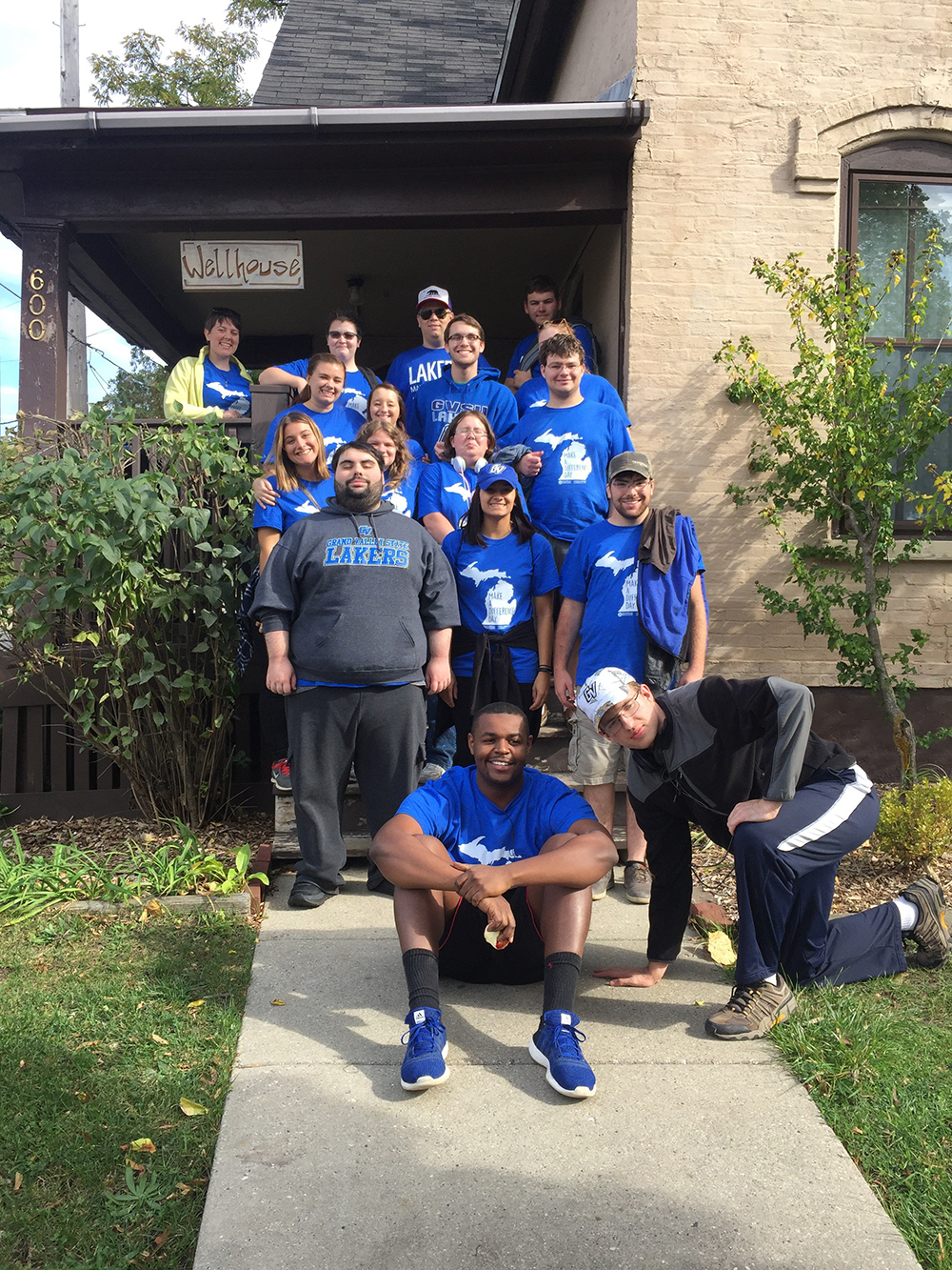 group in blue GVSU Make a Difference Day t-shirts standing on porch and stairs in front of house with Wellhouse sign and number 600 on post