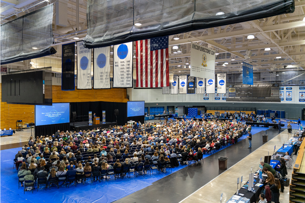 large crowd of people seated in Fieldhouse for presentations