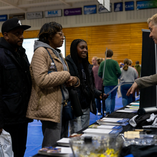 a student and their parents listen to a GVSU staff member across a table at an event in the Fieldhouse