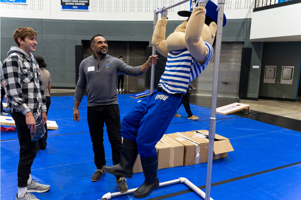 Louie the Laker attempts a pull up while two people look on an laugh