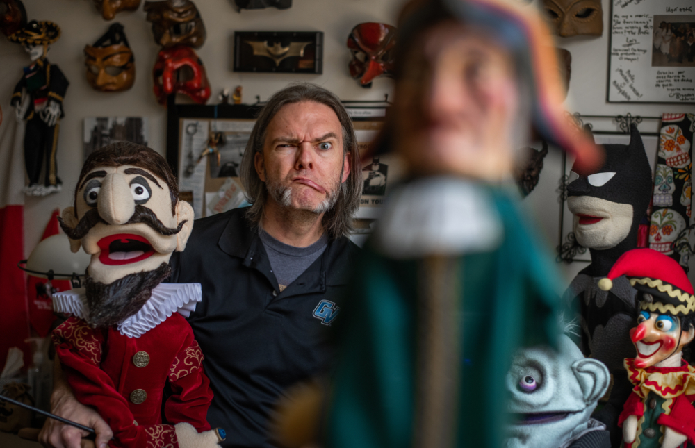 Jason Yancey making funny face behind numerous handmade puppets in his office