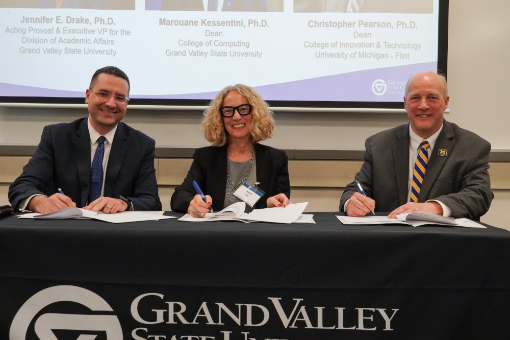 three people seated at table signing documents, GVSU College of Computing table draping