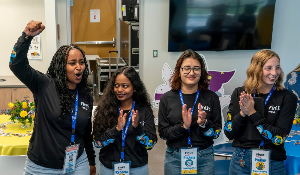 four students in black tshirts clapping; student on left raises arm to pump up crowd
