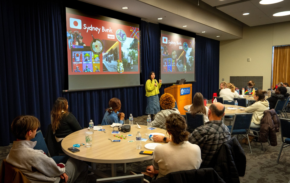 Sydney Bunk shares experiences from a Japan trip before a room of people seated at round tables