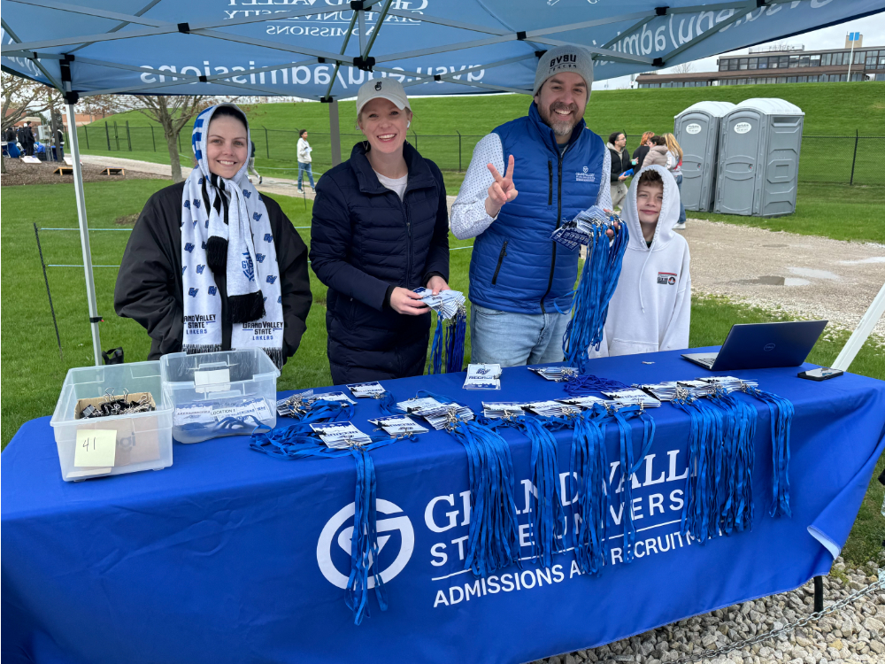 three people and a child standing behind a table with nametags and lanyards under a canopy