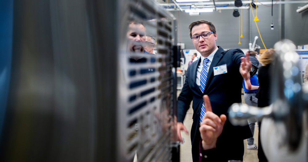 student in suit demonstrates a senior engineering project; the student is positioned between machinery