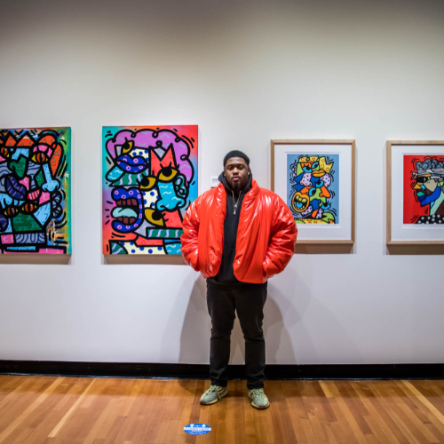 man in puffy red jacket stands in front of colorful artwork in the art gallery