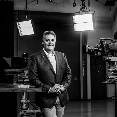 Jim Rademaker stands in the WGVU studios; two lights shine behind him, a camera is pointed at him