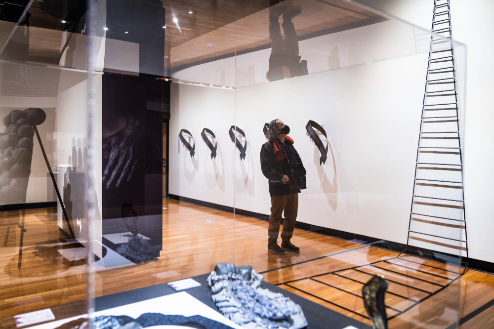 person looks at ladder exhibit within an art display in a gallery room