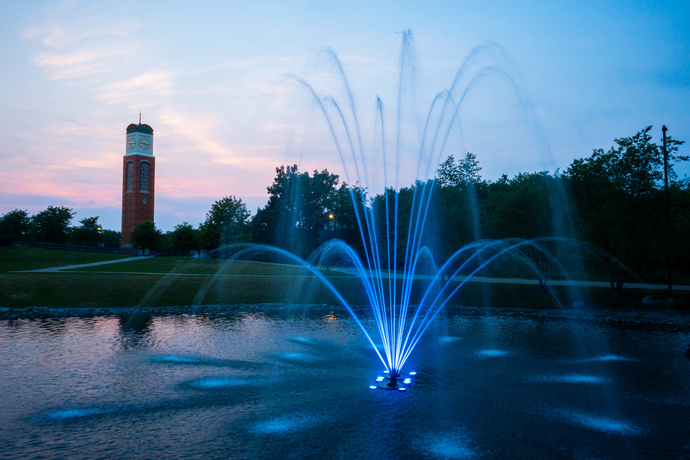 Zumberge Pond fountain lit up in blue, with carillon tower in background during a sunset