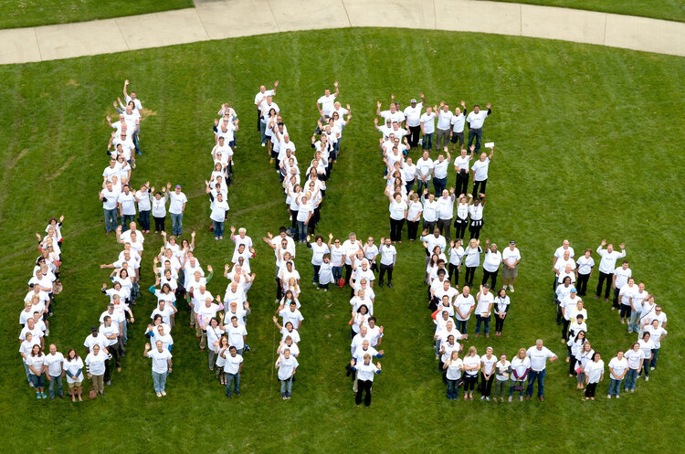 People spelling Live United in a drone photo; they are standing on a field and dressed in white shirts