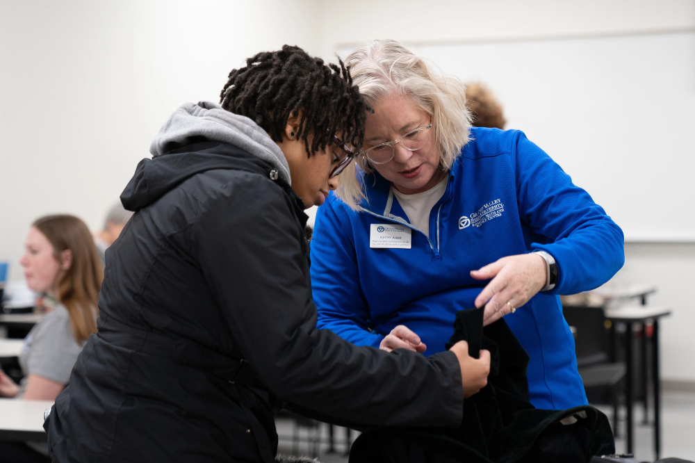 At a previous Repair Clinic, a staff member in a blue jacket looks at an item of clothing with a student, who is dressed in a black jacket