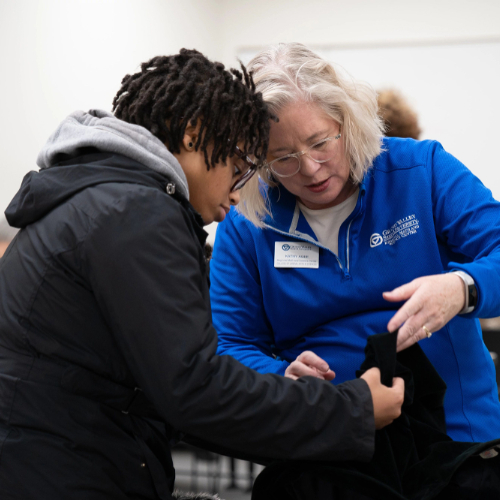 At a previous Repair Clinic, a staff member in a blue jacket looks at an item of clothing with a student, who is dressed in a black jacket