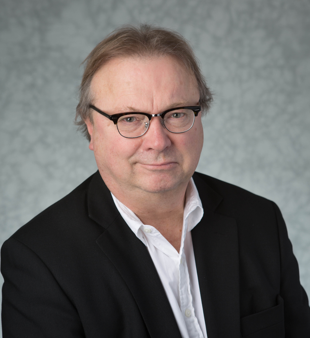 Jim Sanford in dark suit jacket and white shirt, with glasses