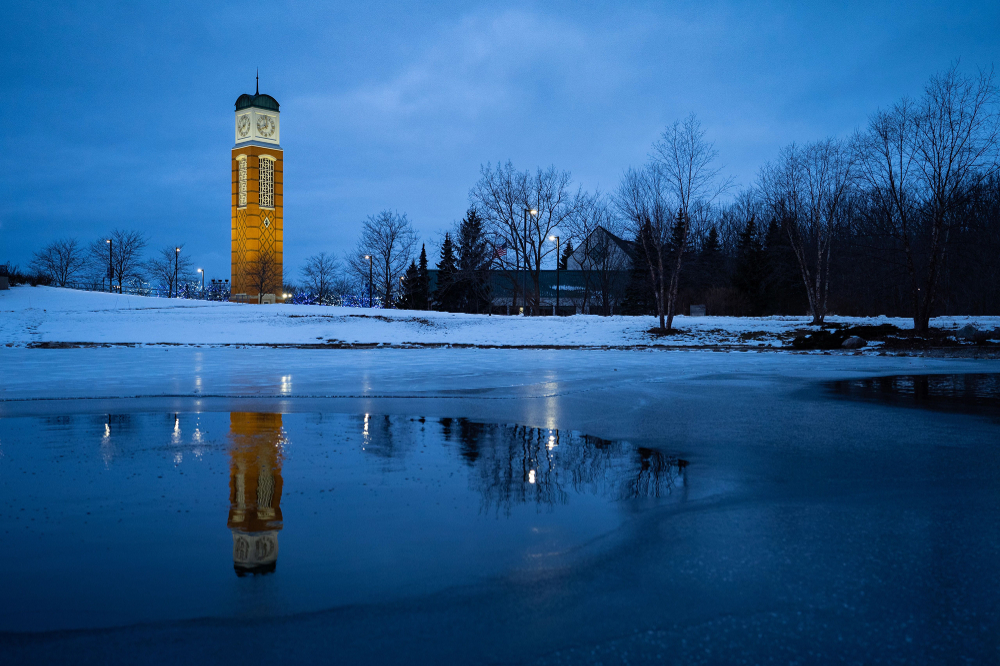 The Cook Carillon Tower reflects in Zumberge Pond, snow covers the ground at night.