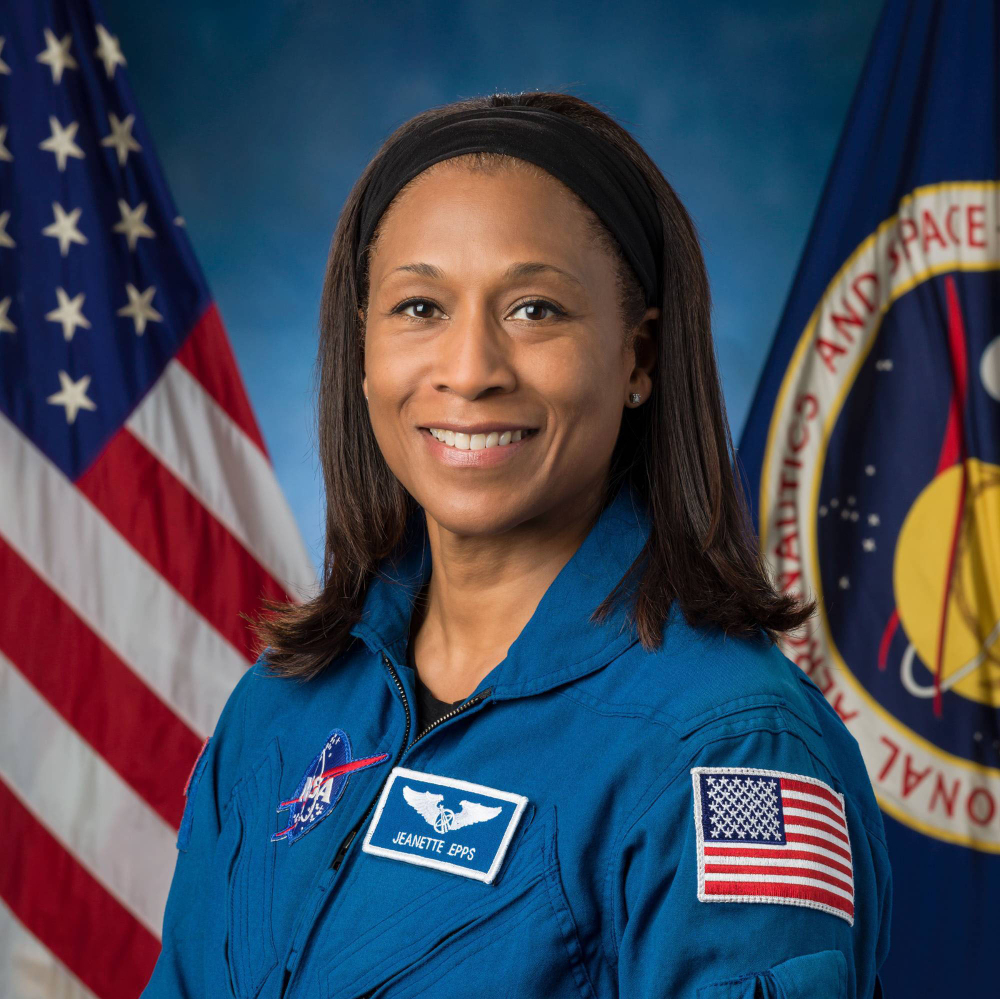 Retired NASA Astronaut Jeanette Epps in blue jumpsuit in front of US and Space Force flags