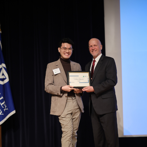 student Jowei Yek in light brown suit accepts a certificate from Jeff Potteiger, who is dressed in a dark suit