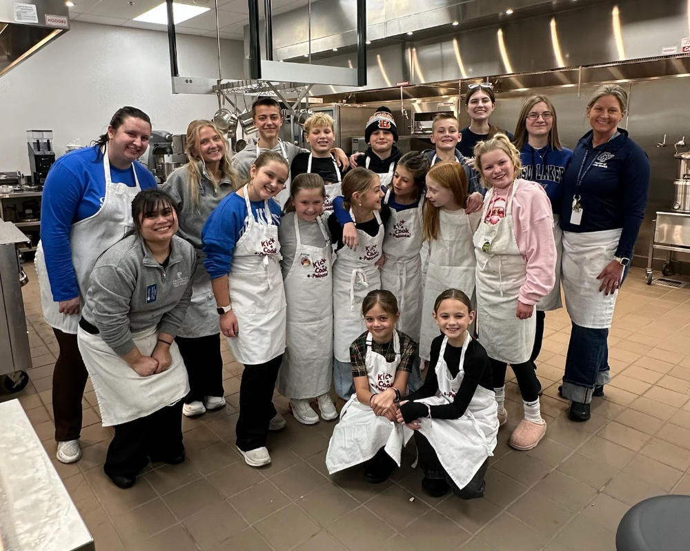 young students, GVSU students and faculty in white aprons in an industrial kitchen in DCIH